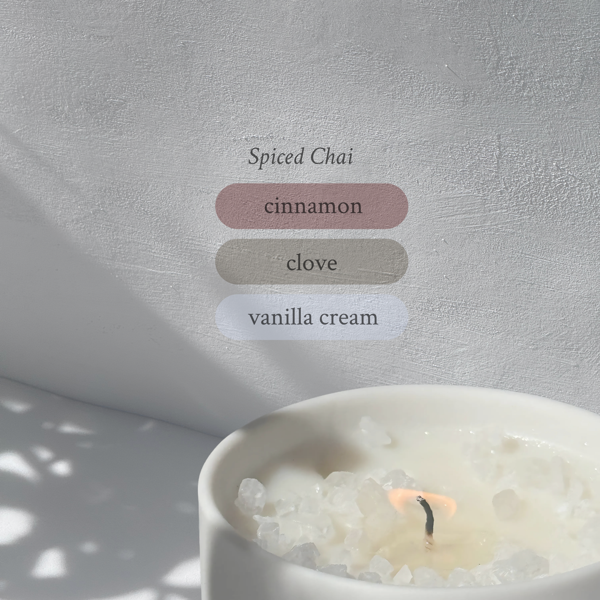 Large stoneware candle, lit, it’s top covered in rock salt. The title reads “Spiced Chai”, and underneath is the scent profile: cinnamon, clove, vanilla cream.