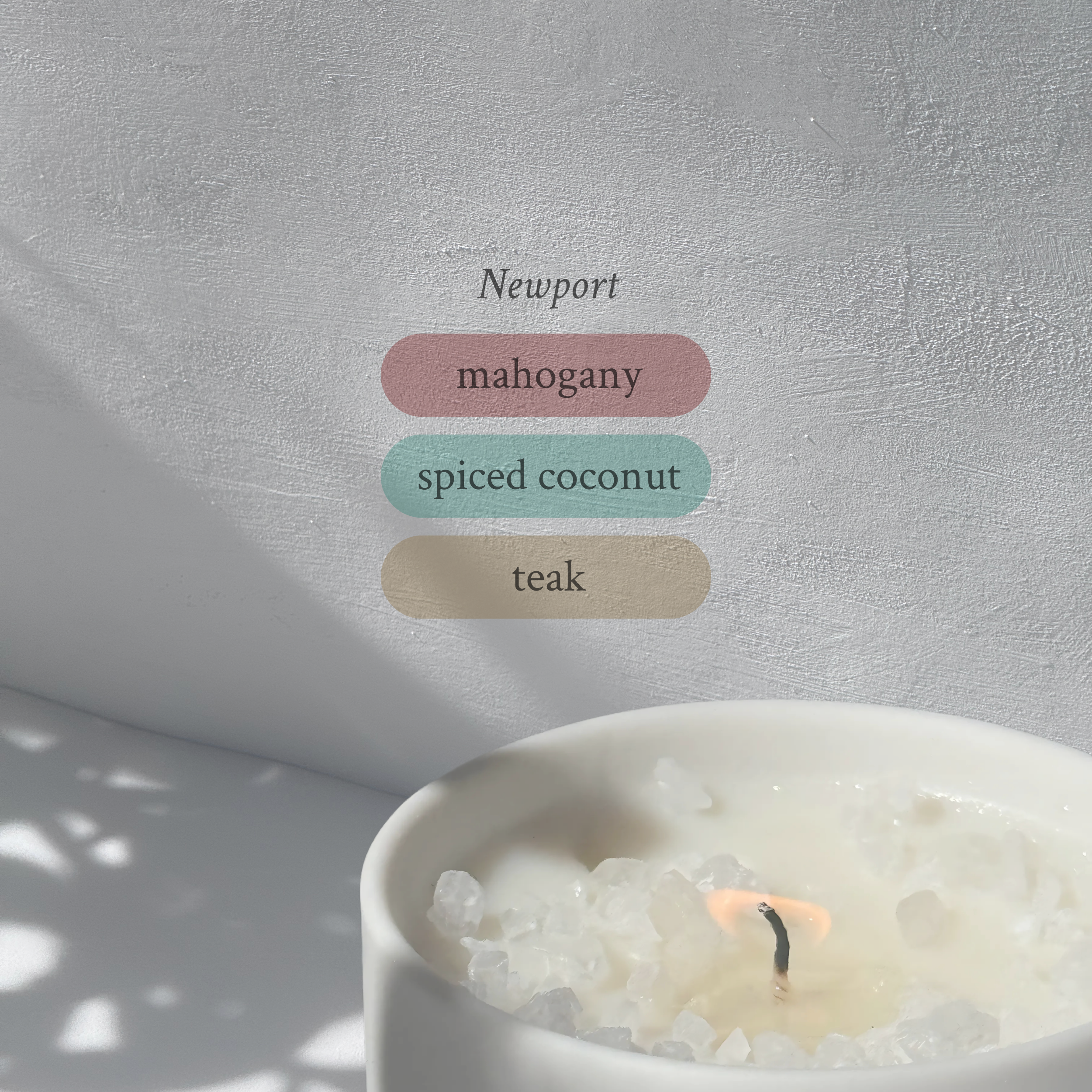 Large stoneware candle, lit, it’s top covered in rock salt. The title reads “Newport”, and underneath is the scent profile: mahogany, spiced coconut, teak.