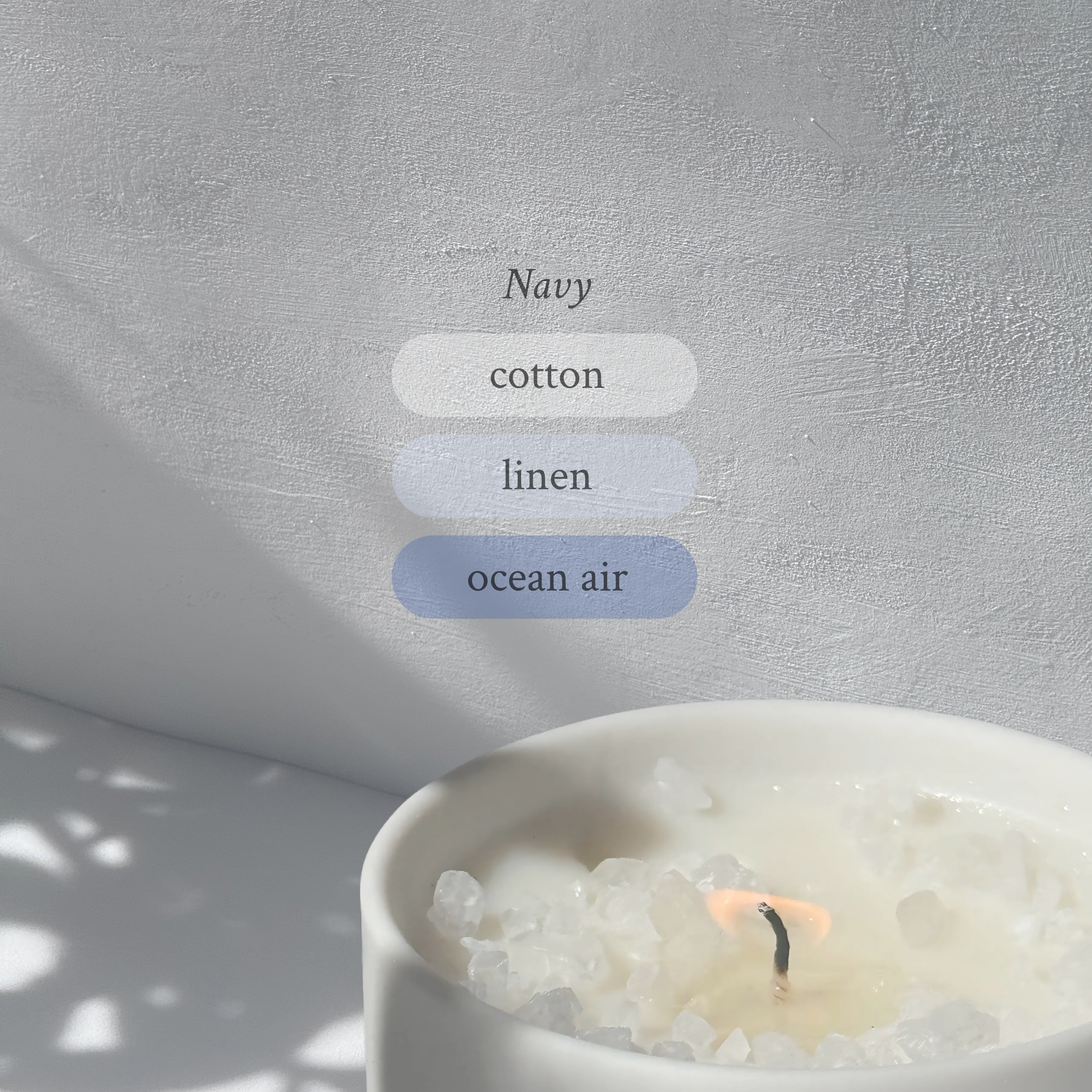 Large stoneware candle, lit, it’s top covered in rock salt. The title reads “Navy”, and underneath is the scent profile: cotton, linen, ocean air.
