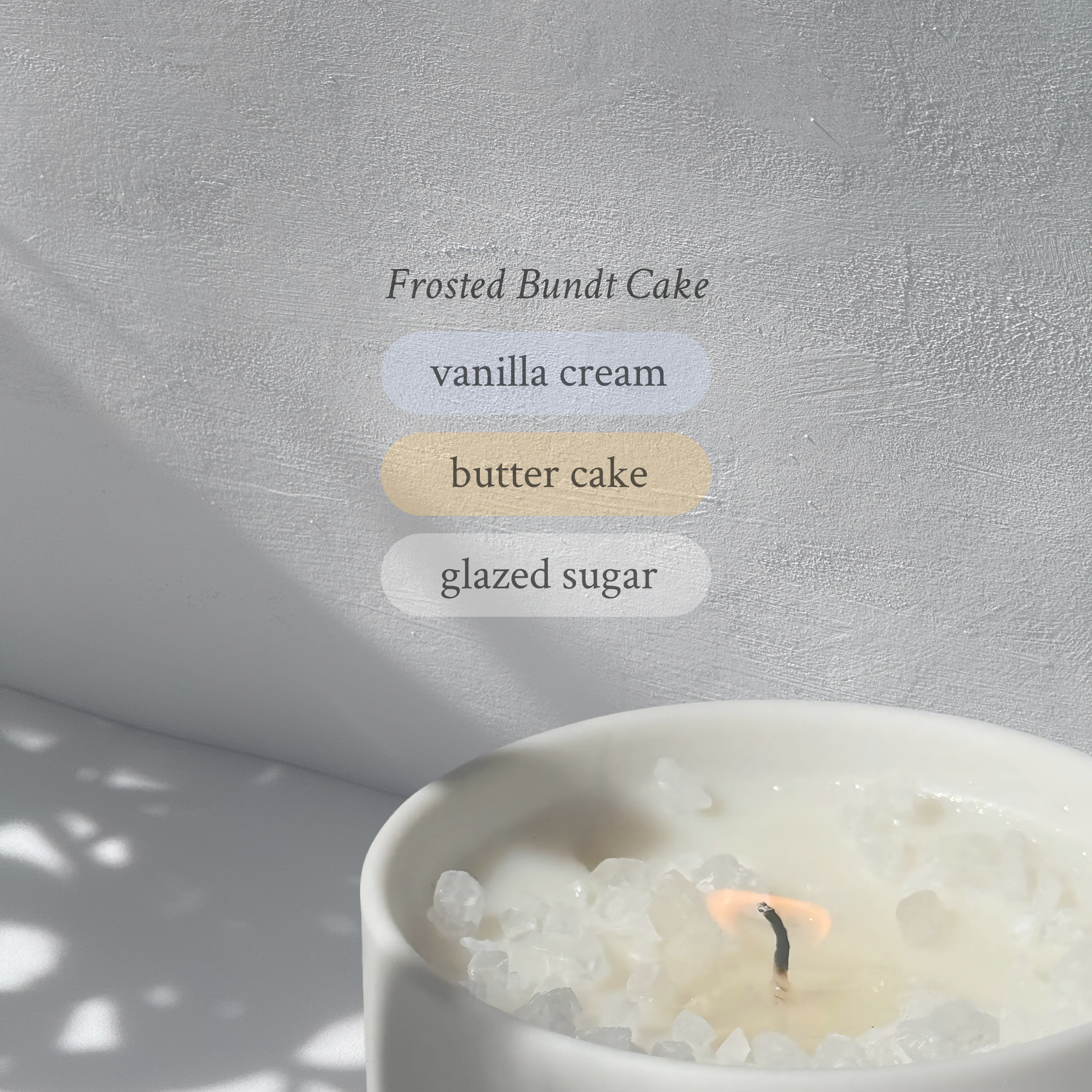 Large stoneware candle, lit, it’s top covered in rock salt. The title reads “Frosted Bundt Cake”, and underneath is the scent profile: vanilla cream, butter cake, glazed sugar.