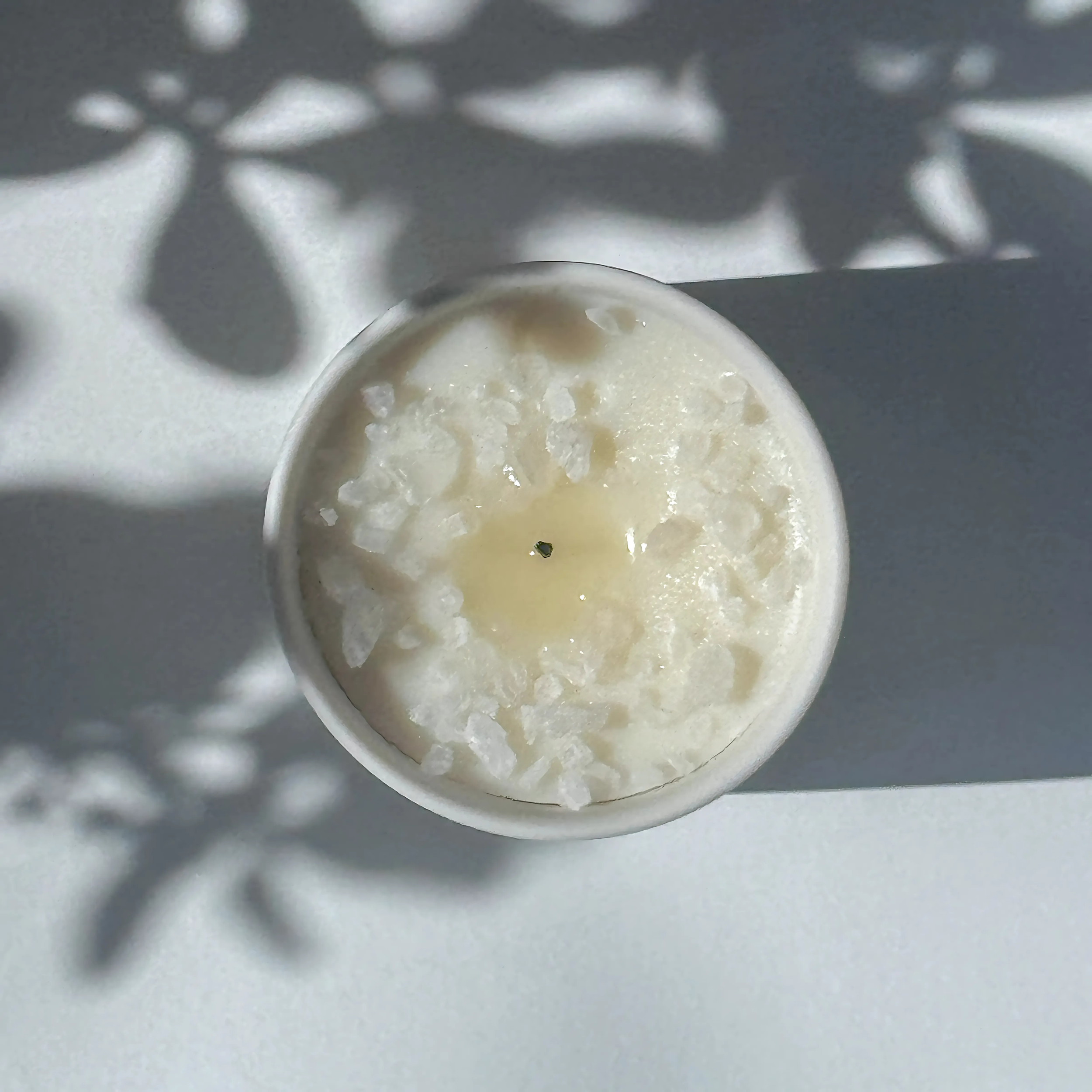 The top of a previously lit candle - its wick is dark, with a small pool of glossy wax in the center, surrounded by crystallized rock salt.