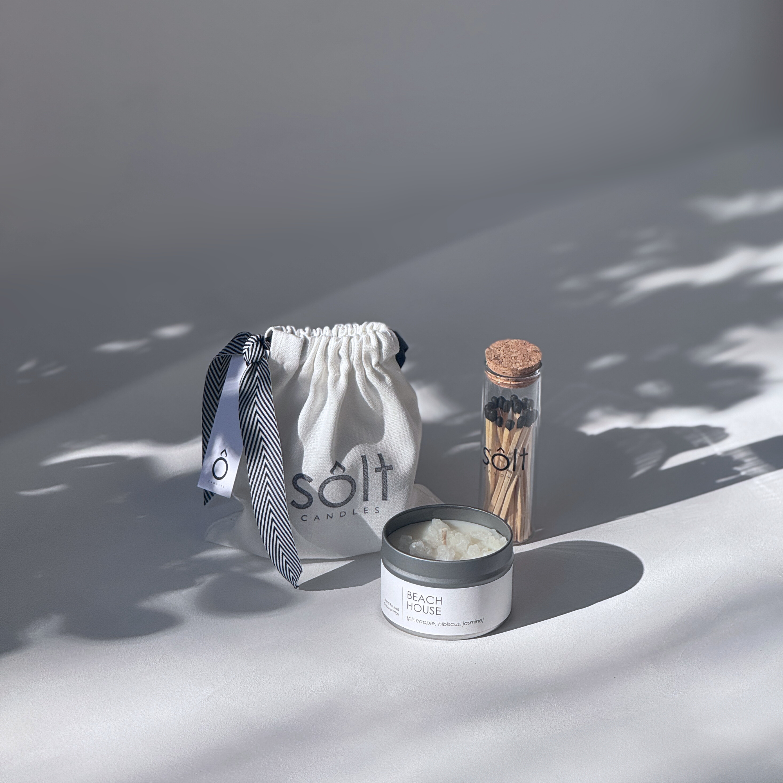 Image of a SOLT gift set, including a mini candle tin covered in crystallized rock salt, a glass jar of matches, and a soft canvas gift bag tied with a ribbon.