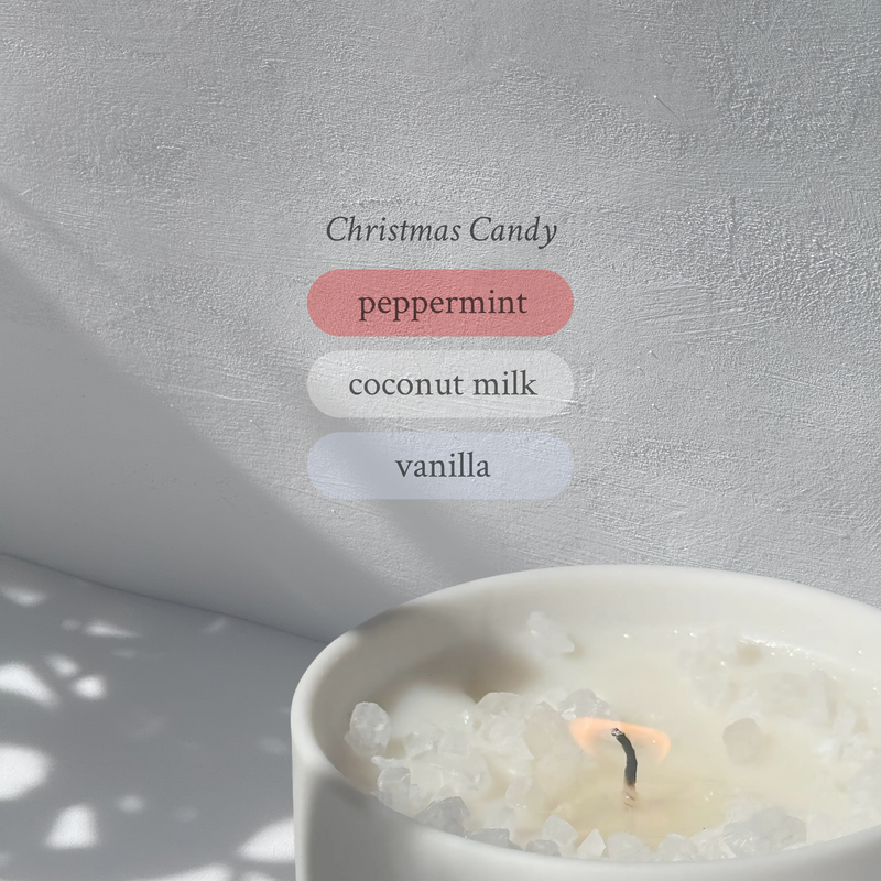 Large stoneware candle, lit, it’s top covered in rock salt. The title reads “Christmas Candy”, and underneath is the scent profile: peppermint, coconut milk, vanilla.
