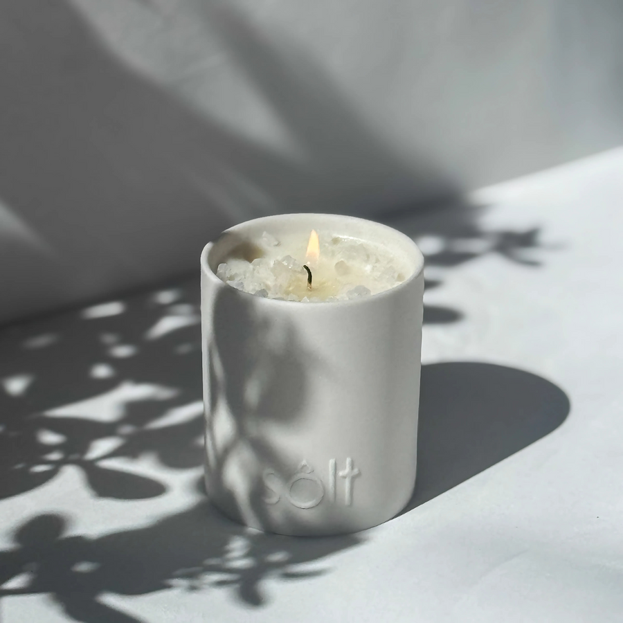 Large stoneware candle, lit in a sun dappled area. The top of the candle is crystallized with rock salt, and a pool of wax grows.