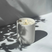 Large stoneware candle, lit in a sun dappled area. The top of the candle is crystallized with rock salt, and a pool of wax grows.