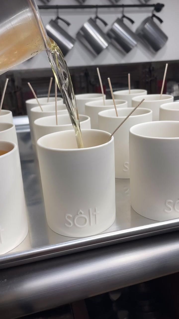 Wax being hand-poured into a row of white stoneware jars